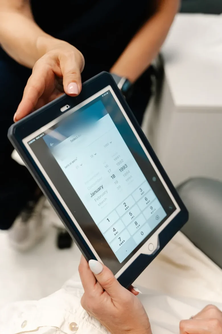 Christine's hands holding a tablet with an intake form toward a seated client